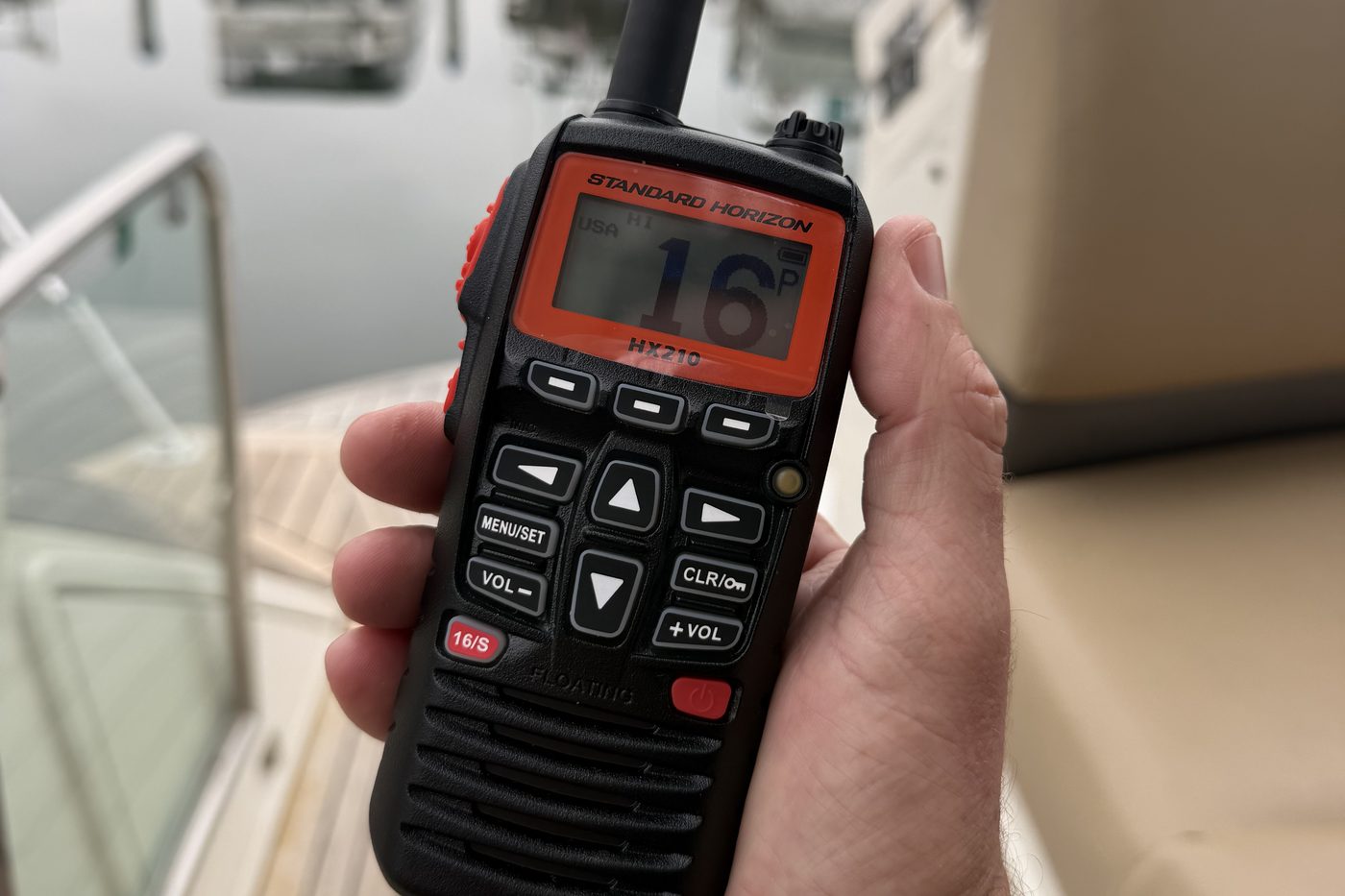 A Standard Horizon HX210 handheld VHF radio held on the dock, tuned to Channel 16